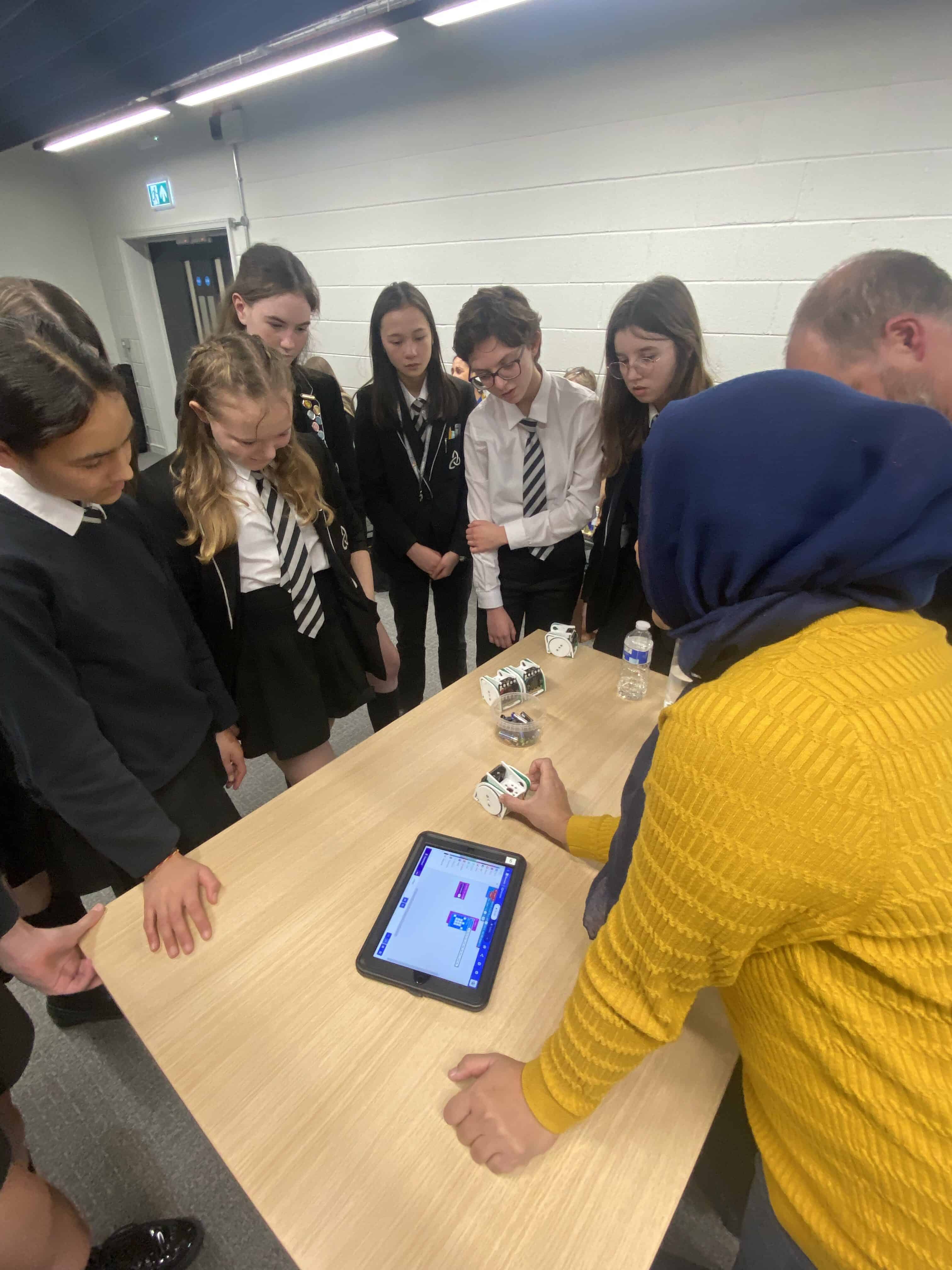 A group of Laurus Ryecroft students gather around a table and watch a demonstration for an activity at the Cyber First Girls event