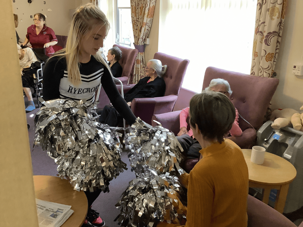 A student from Laurus Ryecroft hands a cheerleading pom pom to a resident from Hurst Hall Care Home