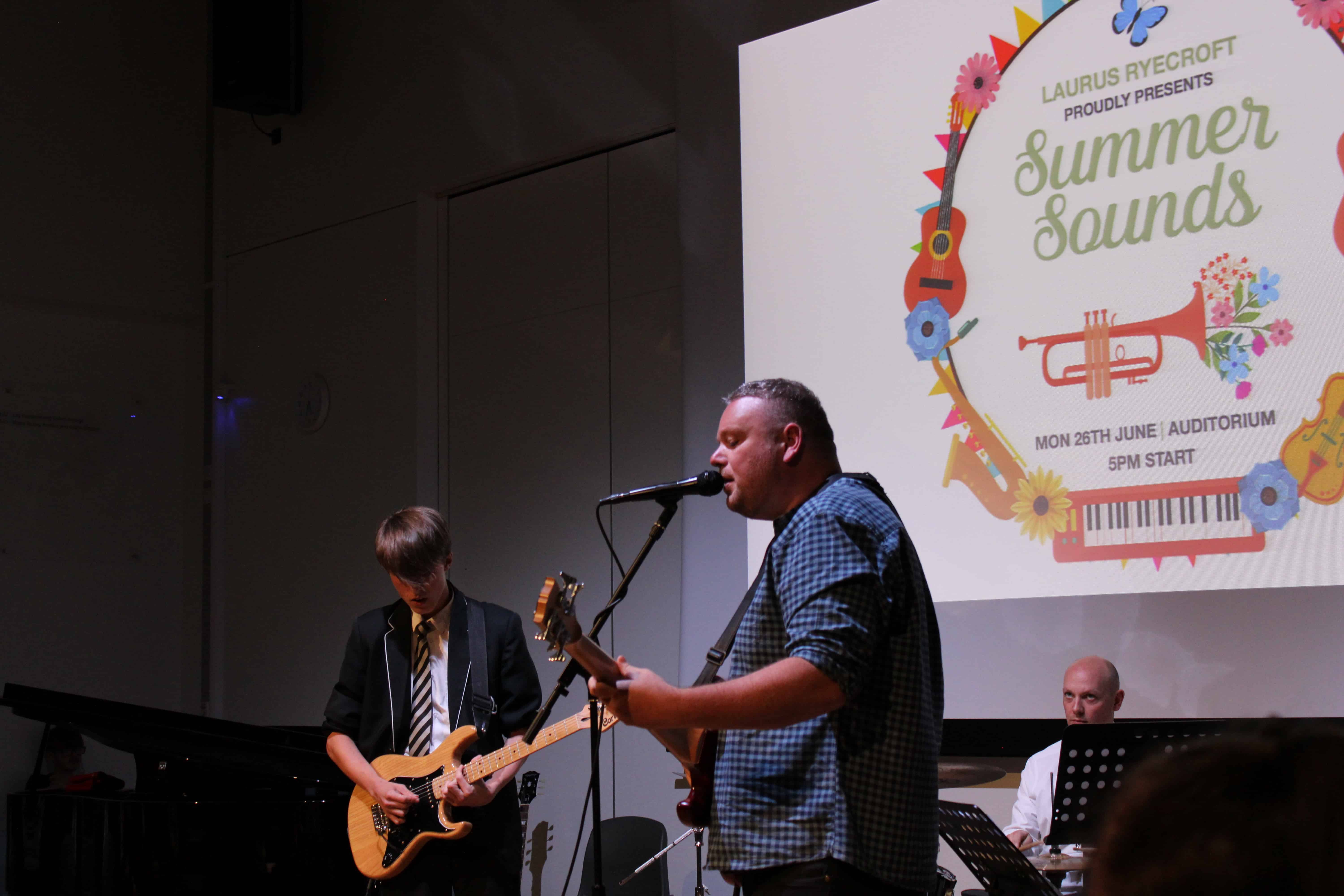 A Laurus Ryecroft student and a man play guitar and sing together during Summer Sounds 2023