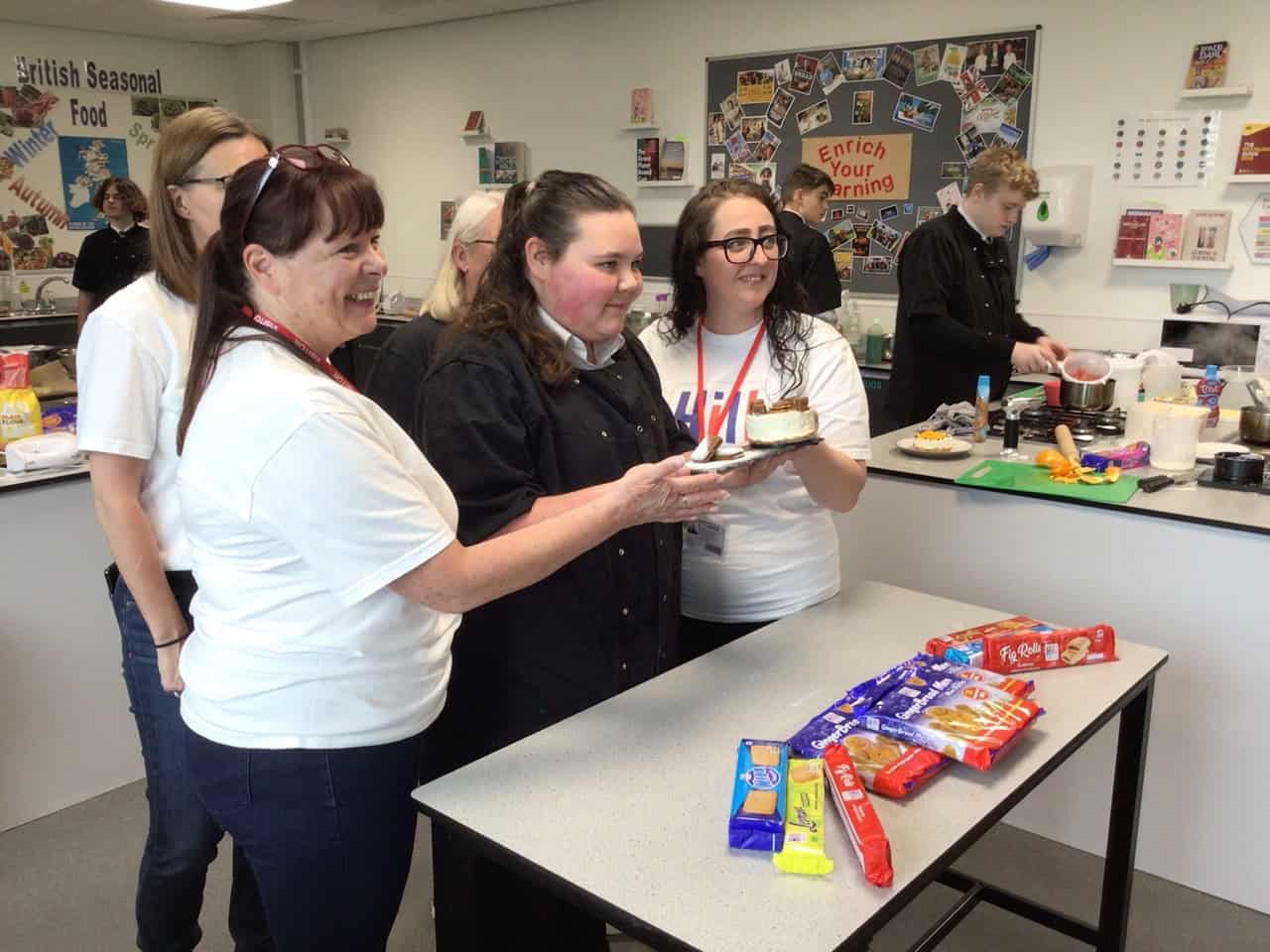 The winning student stands with Hill Biscuits staff and holds her cheesecake at Laurus Ryecroft on National Biscuit Day.
