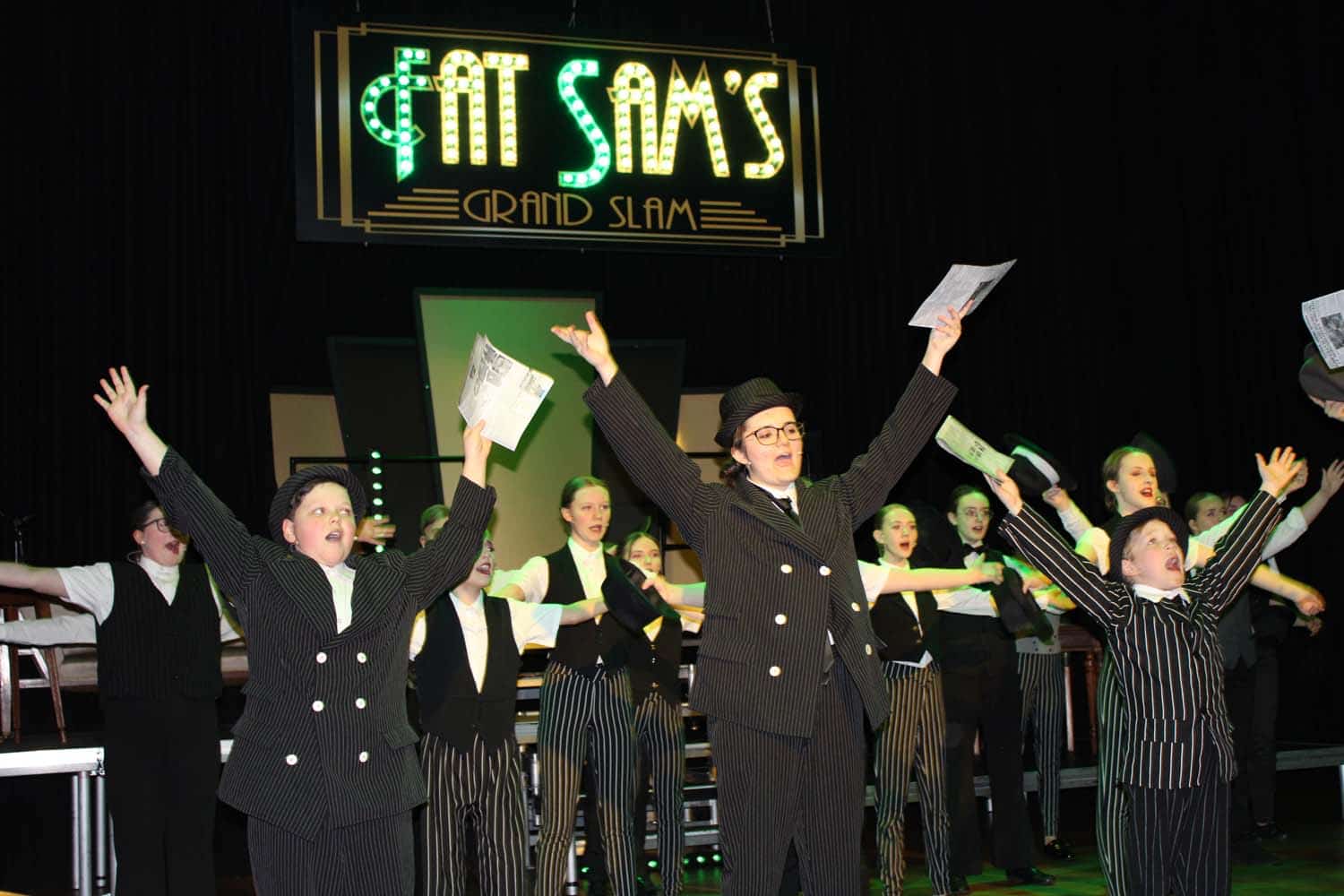 Students raise their arms as they sing at Fat Sam's Grand Slam in the Laurus Ryecroft production of Bugsy Malone.