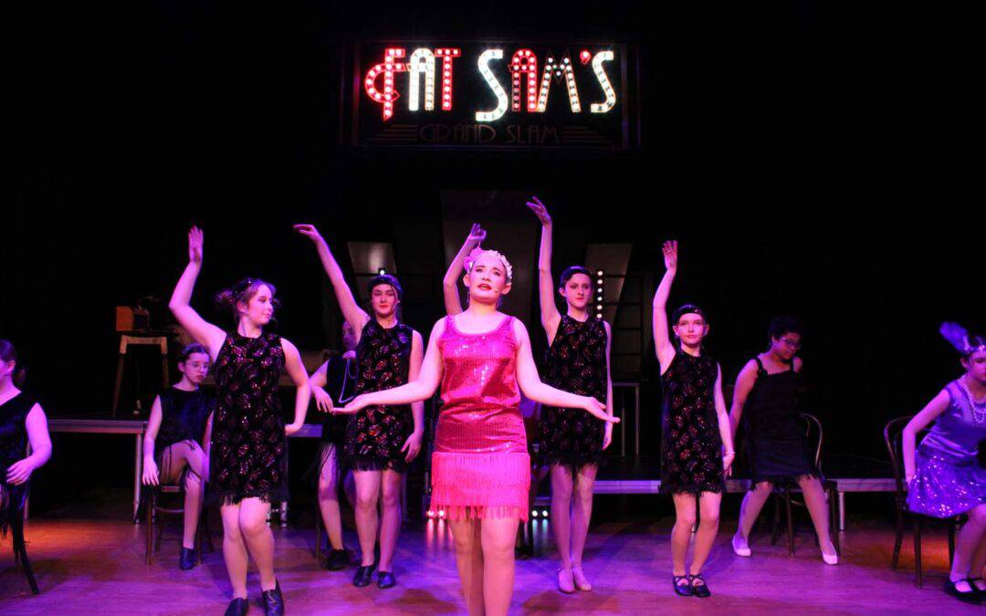 Students do a choreographed dance led by Tallulah in front of Fat Sam's in the Laurus Ryecroft production of Bugsy Malone.