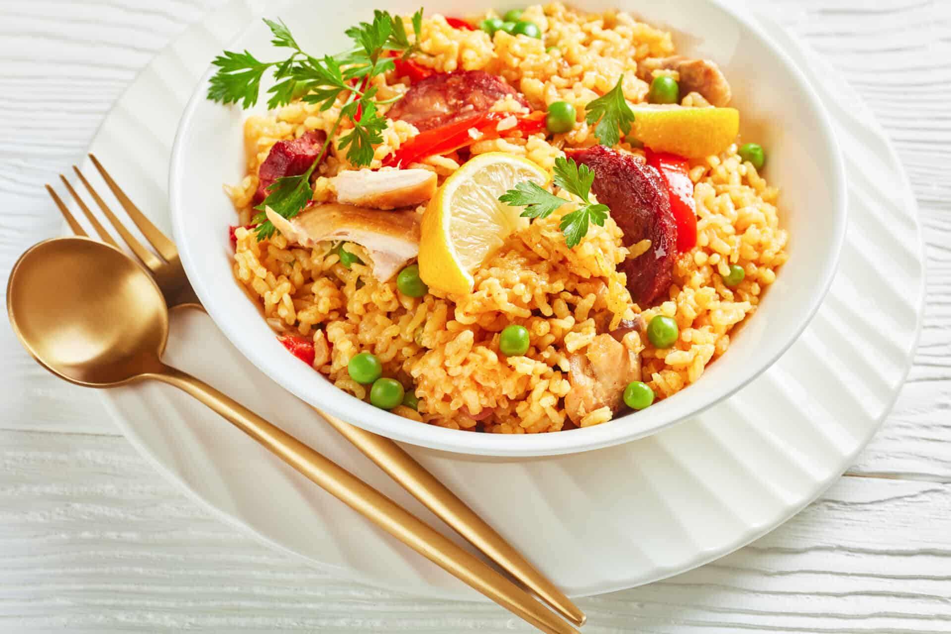 An example of Dolce food served in Laurus Ryecroft canteen. A close-up of spanish chicken paella with valencian bomba rice, chicken thigh meat, chorizo sausages, vegetables and spices served on a white plate on a white wooden table