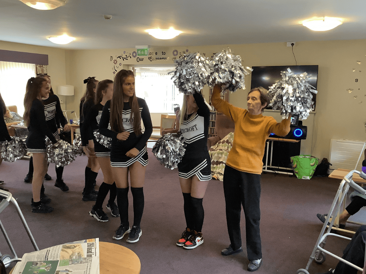 Student cheerleaders from Laurus Ryecroft perform with a resident at Hurst Hall Care Home.